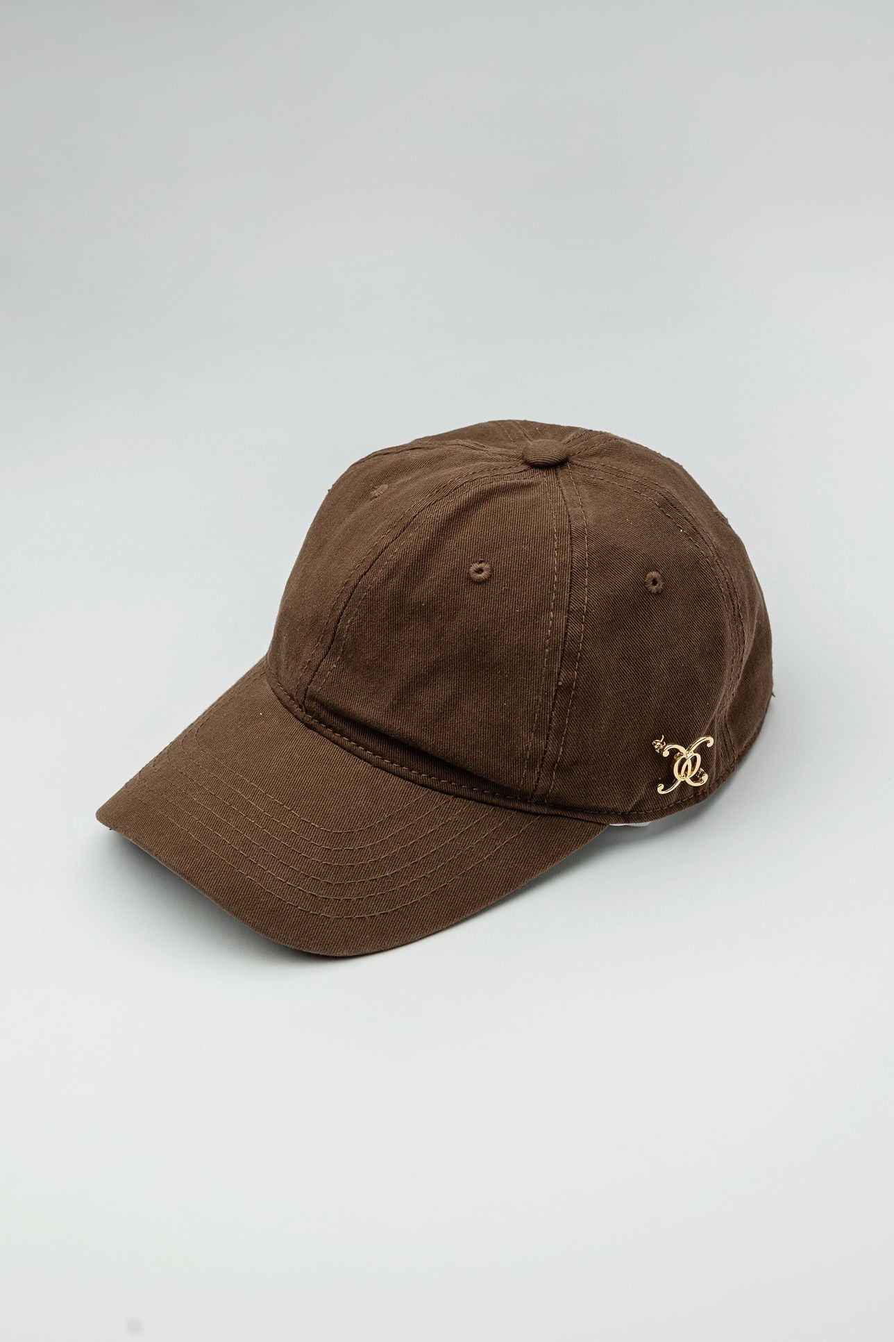 A brown baseball cap with a gold-plated logo on the front.
