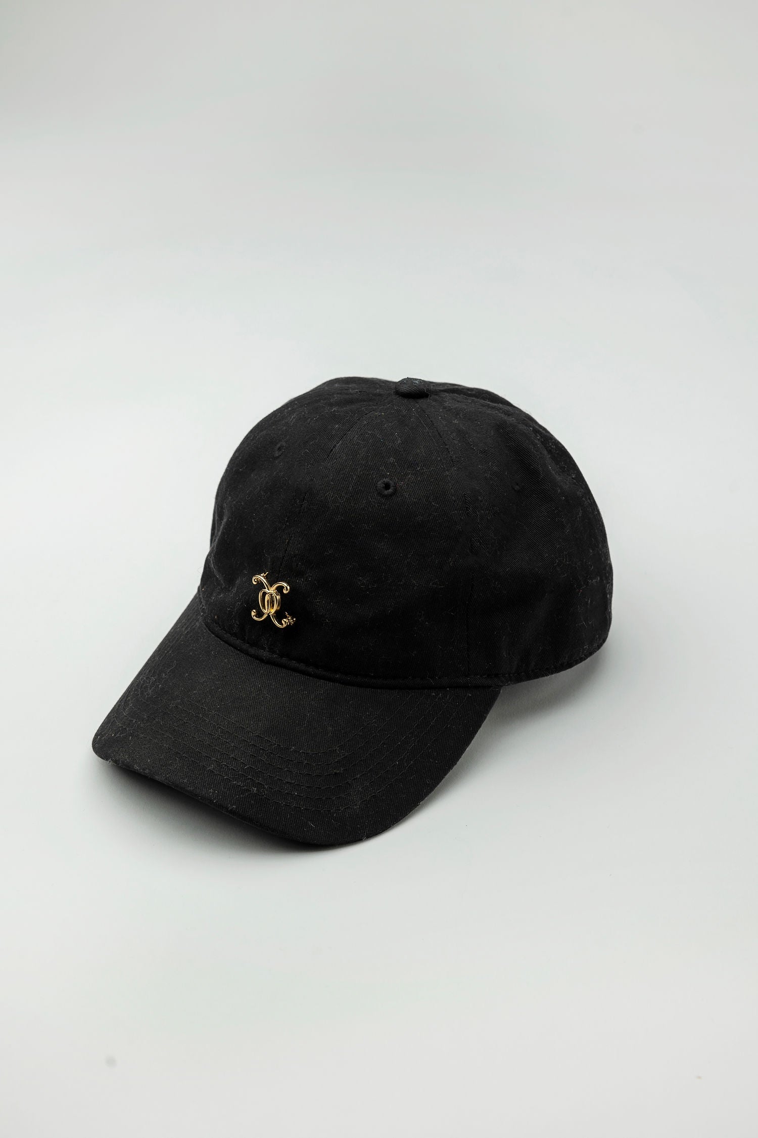 A black baseball cap with a gold-plated logo on the front.